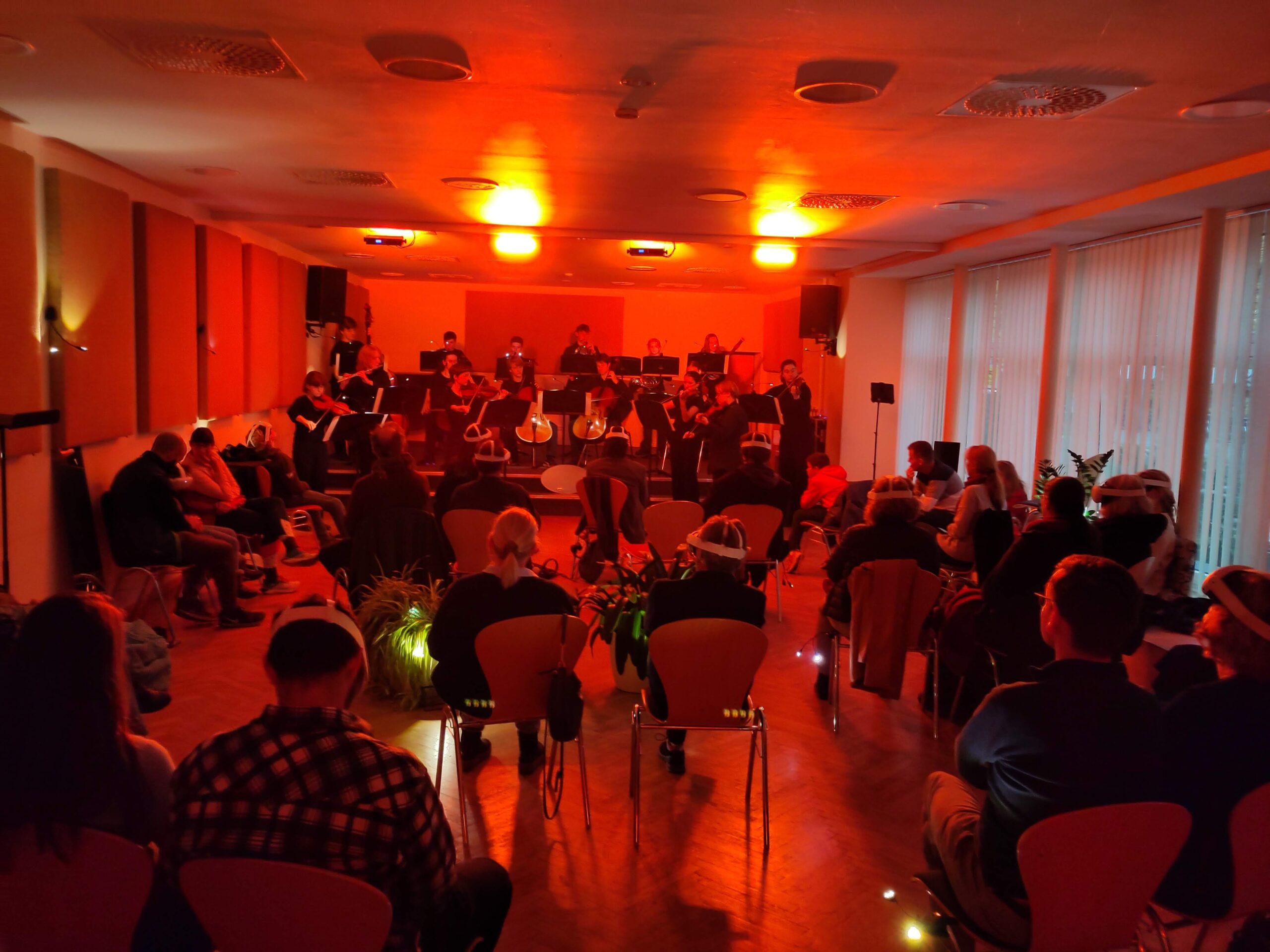 Ein kleinerer Veranstaltungsraum in rotes Licht getaucht. Eine Bühne mit einer Band und Publikum.